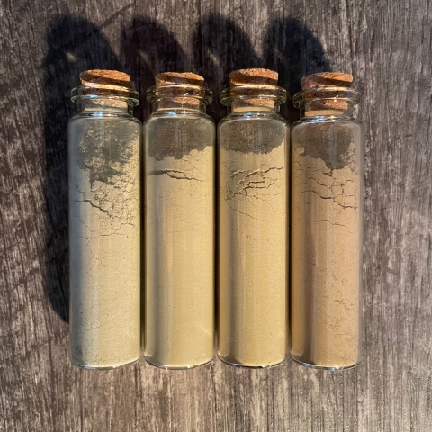 Four different coloured pigments in glass vials with cork stoppers.